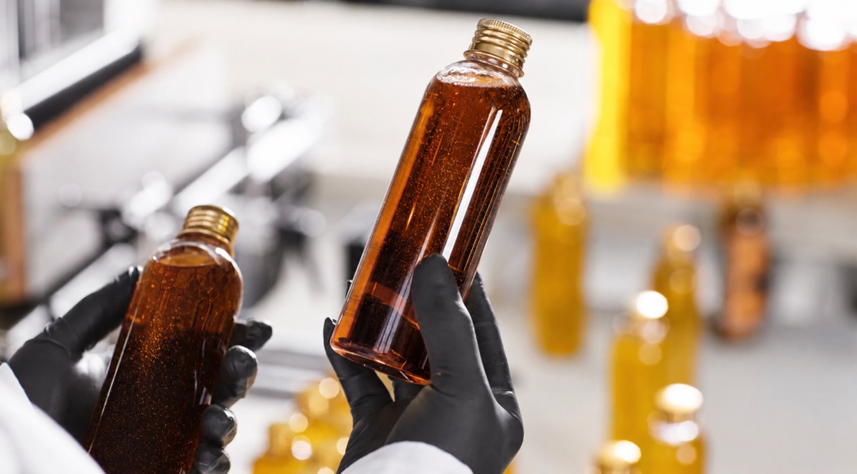 Gloved hands holding amber liquid bottles for residue oil and vegetable pitch applications